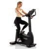 Na zdjęciu znajduje się rower elektromagnetyczny z osobą ćwiczącą na nim, z widocznym logo "HAMMER Maximum" na obudowie. Rower ma ciemną konstrukcję z wyświetlaczem i uchwytami.