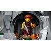 Na obrazie znajduje się figurka LEGO wikinga w jaskini, trzymająca młot i okrągły przedmiot, otoczona klockami imitującymi kamienie i ziemię. W tle widoczna jest szczegółowa konstrukcja z szarych klocków, tworząca łukowate wejście do jaskini.
