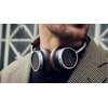 Na zdjęciu widoczne są brązowe słuchawki nauszne z napisem "BEYERDYNAMIC" na nausznikach, noszone przez osobę w marynarce w kratę. W tle znajduje się rozmyty wzór geometryczny.