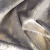 Tkanina zasłony w kolorze stalowo-złotym z widocznymi refleksami świetlnymi, tworząca efekt połysku. Materiał ma delikatną teksturę i nieregularne wzory.