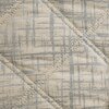 Narzuta w kolorze kremowym o wymiarach 220 x 240 cm pokrywa łóżko, prezentując wzór w delikatne, geometryczne linie. W tle widoczne są dwie białe poduszki, lampa z metaliczną podstawą oraz zegar na stoliku nocnym.
