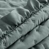 Zdjęcie przedstawia fragment jasnozielonej narzuty z widocznym pikowaniem w kształcie małych krzyżyków. Materiał ma delikatną fakturę, która nadaje mu elegancki wygląd.