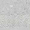 Srebrny ręcznik o wymiarach 30 x 50 cm z widoczną teksturą, składającą się z dwóch części: górnej z drobnym, gęstym splotem oraz dolnej z wzorem w jodełkę.