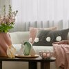 Na zdjęciu znajduje się jasna sofa z dwoma poduszkami, jedna z nich to "Poszewka EUROFIRANY 467106 Wiosna 54 30 x 50 cm Pudrowy", a obok niej stoi stolik z dekoracyjnymi jajkami i wazonem z różowymi kwiatami. W tle widać białą zasłonę, a na sofie leży róż