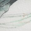 Fragment jasnoszarej pościeli z delikatnym, abstrakcyjnym wzorem w odcieniach zieleni i szarości. Widoczne jest logo "EVA MINGE" w kolorze beżowym.