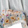 Biała firana z delikatnego materiału ozdobiona jest kolorowym wzorem przedstawiającym kwiaty w odcieniach pomarańczowego, różowego, niebieskiego i fioletowego. Dolna krawędź firany wykończona jest białą koronką.