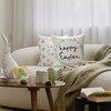 Na zdjęciu znajduje się jasna sofa z dwiema poduszkami, na których widnieje napis "happy Easter" oraz wzory w pastelowych kolorach. Przed sofą stoi drewniany stolik z dekoracjami wielkanocnymi, w tym figurką królika i kolorowymi jajkami.