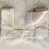 Zbliżenie na zasłonę z beżowym wzorem w liście na jasnym tle, z widocznymi zakładkami i rzepem do mocowania. Materiał ma delikatną teksturę i subtelny wzór w jodełkę.