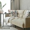 Beżowa sofa z dwoma poduszkami ozdobionymi kwiatowym wzorem w odcieniach niebieskiego i zielonego stoi na drewnianej podłodze. Obok sofy znajduje się czarny stolik z wazonem z zielonymi gałązkami, a w tle widać zasłony i lampę stojącą.