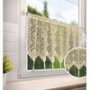 Jasnobeżowa firana gotowa o wymiarach 150 x 60 cm wisi na oknie, prezentując ażurowy wzór z motywami roślinnymi i zakończona jest frędzlami. W tle widoczny jest rozmyty krajobraz z zielenią.