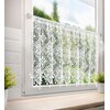 Biała firana o wymiarach 150 x 60 cm wisi na oknie, prezentując ażurowy wzór z motywem roślinnym. W tle widoczny jest rozmyty widok zieleni za oknem, a na parapecie stoją dwie doniczki z roślinami.