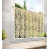 Beżowa firana o wymiarach 150 x 60 cm wisi na oknie, prezentując ażurowy wzór z motywami roślinnymi. Na parapecie znajdują się dwie doniczki z zielonymi roślinami, a za oknem widać rozmyty krajobraz z drzewami.