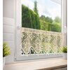 Beżowa firana o wymiarach 150 x 30 cm wisi na oknie, wykonana z ażurowego materiału z ozdobnym wzorem. Na parapecie znajdują się dwie doniczki z zielonymi roślinami, a za oknem widoczny jest rozmyty krajobraz z drzewami.