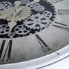 Zbliżenie na tarczę zegara ściennego z widocznymi ozdobnymi zębatkami i wskazówkami w stylu retro. Na tarczy znajdują się rzymskie cyfry, a całość utrzymana jest w biało-czarnej kolorystyce z efektem postarzenia.