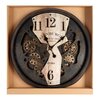 Na zdjęciu znajduje się okrągły zegar ścienny z widocznymi zębatkami w tle, umieszczony w kartonowym opakowaniu. Na tarczy zegara widnieje napis "EDINBURGH CLOCK WORKS COMPANY" oraz "EST. 1923", a cyfry godzinowe są duże i wyraźne.
