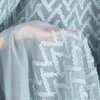 Zdjęcie przedstawia fragment niebieskiej zasłony z wyraźnym, wypukłym wzorem w zygzaki. Tkanina jest półprzezroczysta, co pozwala na delikatne przenikanie światła.