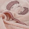 Różowa myjka kąpielowa z miękkiego materiału, ozdobiona haftem przedstawiającym jeża. Krawędzie myjki wykończone są ciemniejszym różowym obszyciem.