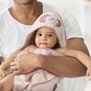 Na zdjęciu widoczny jest różowy ręcznik z kapturem, ozdobiony haftem przedstawiającym dwa jeże. Ręcznik ma obszycie w odcieniu różowym i jest trzymany przez osobę w białej koszulce.
