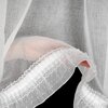 Biała firana z delikatnego materiału, ozdobiona koronkowym brzegiem i drobnymi kropkami, jest uchwycona w zbliżeniu. W tle widoczna jest struktura tkaniny, przez którą prześwituje światło.
