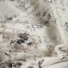 Zasłona w kolorze kremowym z nieregularnym wzorem w odcieniach brązu i czerni, układająca się w miękkie fałdy. Materiał ma teksturę z widocznymi kontrastowymi plamami.