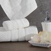 Na zdjęciu widoczny jest kremowy ręcznik o wymiarach 30 x 50 cm, z delikatnym wzorem w paski i teksturą. Obok ręcznika znajduje się dozownik na mydło w płynie oraz mydelniczka z gąbką i kulką soli do kąpieli, ustawione na tle szarej ściany.