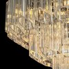 Zdjęcie przedstawia fragment lampy sufitowej z przezroczystymi, pionowymi elementami szklanymi, które odbijają światło, tworząc efektowne refleksy. W tle widoczny jest czarny kolor, który podkreśla blask i detale lampy.