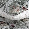 Pościel przedstawiona na zdjęciu ma biały kolor z wzorem roślinnym w odcieniach zieleni, różu i szarości. Na łóżku znajdują się dwie poduszki i kołdra, które mają ten sam wzór.