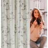 Zasłona EUROFIRANY Selena 140 x 270 cm w kolorze kremowo-szampańskim z delikatnym kwiatowym wzorem. Obok zasłony widoczna jest osoba trzymająca czarny kubek.