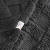 Zdjęcie przedstawia fragment stalowego koca o teksturze przypominającej futro, z widoczną metką z napisem "design 91 for your home". Koc ma wyraźną, puszystą strukturę, a metka jest przyszyta do jego krawędzi.