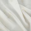 Zdjęcie przedstawia fragment materiału zasłony w kolorze naturalno-szampańskim z delikatnym, złotym wzorem. Tkanina ma lekko połyskującą powierzchnię i jest ułożona w miękkie fałdy.
