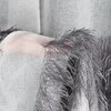 Biała zasłona z delikatnym, srebrnym wzorem i ozdobnymi frędzlami w kolorze szarym. Materiał ma lekko przezroczystą strukturę, co nadaje mu elegancki wygląd.