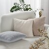 Na zdjęciu znajduje się jasna sofa z trzema poduszkami o teksturowanej powierzchni w kolorach srebrnym, białym i beżowym. W tle widoczne są zielone liście rośliny oraz złota dekoracja w kształcie twarzy.