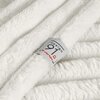 Na zdjęciu widoczny jest biały koc o puszystej fakturze, z metką z napisem "design 91 for your home". Koc jest złożony, co podkreśla jego miękkość i strukturę materiału.