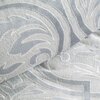 Zdjęcie przedstawia fragment pościeli o srebrnym kolorze z wyraźnym, wypukłym wzorem w kształcie liści i krzywizn. Materiał ma teksturę przypominającą miękki, pluszowy materiał.