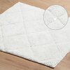 Zdjęcie przedstawia fragment białego, prostokątnego dywanika łazienkowego o puszystej fakturze. Powierzchnia dywanika ma wzór w kształcie rombów, co nadaje mu elegancki wygląd.