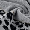Srebrny ręcznik o wymiarach 70 x 140 cm z widoczną teksturą frotte, złożony w sposób tworzący miękkie fałdy. Na brzegu ręcznika znajduje się wzór w czarne plamy na białym tle, oddzielony brązową lamówką.
