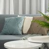 Na zdjęciu widoczna jest szara sofa z trzema poduszkami w poszewkach w kolorach niebieskim, kremowym i brązowym, a obok znajduje się biały, okrągły stolik. W tle widać szare zasłony, a na pierwszym planie zieloną roślinę.