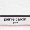 Biały ręcznik z widoczną metką, na której znajduje się napis "pierre cardin paris" otoczony czerwonym i czarnym paskiem. Tkanina ręcznika ma delikatną fakturę.