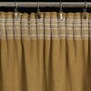 Zasłona w kolorze miodowym zawieszona na metalowym karniszu za pomocą metalowych klipsów. Górna część zasłony ma przezroczysty pas z poziomymi liniami.