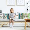 Na zdjęciu znajduje się jasna sofa z kilkoma poduszkami ozdobionymi wizerunkami uśmiechniętych zwierząt, w tym lam. W tle widoczne są dwa obrazki w ramkach, jeden z kropkami, a drugi z prostym rysunkiem twarzy zwierzęcia.