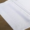 Biały obrus o wymiarach 85 x 85 cm leży na drewnianym stole, ukazując gładką powierzchnię i starannie wykończone brzegi. Materiał jest równomiernie rozłożony, tworząc elegancki i schludny wygląd.