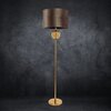 Brązowo-złota lampa podłogowa o wysokości 165 cm, z okrągłym abażurem i ozdobnym elementem na złotym trzonku, stoi na ciemnym tle. Produkt to "Lampa podłogowa EUROFIRANY Leona 467321".