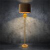 Lampa podłogowa o wysokości 165 cm z brązowo-złotym wykończeniem, z okrągłym kloszem i dekoracyjną kulą pod kloszem, stoi na tle szarej, teksturowanej ściany. Światło lampy tworzy jasną poświatę na ścianie.