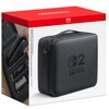 Kwadratowe pudełko z czerwonym wieczkiem zawiera czarną walizkę z napisem "NINTENDO SWITCH" oraz cyfrą "2". Na boku opakowania widoczna jest ilustracja przedstawiająca wnętrze walizki z miejscem na konsolę i akcesoria.