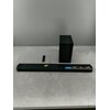 Na zdjęciu znajduje się czarny soundbar z widocznymi naklejkami informacyjnymi oraz bezprzewodowy subwoofer. Obok soundbara leży pilot, a na naklejkach widnieją napisy: "DTS Virtual:X", "Bluetooth", "5.1 Channel".