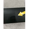 Czarny soundbar z widoczną żółtą strzałką na powierzchni, leży na szarej wykładzinie.