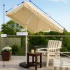 Beżowy parasol ogrodowy o wymiarach 200 cm na 120 cm i wysokości 210 cm, z rurą o średnicy 28/32 mm, stoi na tarasie obok drewnianego stolika, fotela i donicy z kwiatami, na tle zieleni.