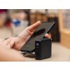 Na zdjęciu widać czarny powerbank z wyświetlaczem pokazującym "60" oraz dwoma portami USB, obok którego znajduje się smartfon. W tle widoczne są rozmyte elementy wnętrza.