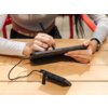 Na zdjęciu widać osobę trzymającą tablet i rysującą na nim rysikiem, a obok na stole leży podłączony powerbank z widocznymi oznaczeniami CE i innymi symbolami. Tablet ma trzy widoczne przyciski na boku, a powerbank jest podłączony do tabletu za pomocą kab