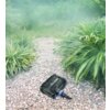 Na zdjęciu widać elektryczną pompę AQUACRAFT Sub Eko 10000 umieszczoną na żwirowej ścieżce otoczonej bujną zielenią. Produkt ma czarną obudowę z niebieskimi elementami.